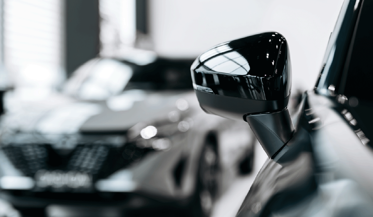 Close-up of a car's side mirror with a blurred car in the background inside a showroom or garage