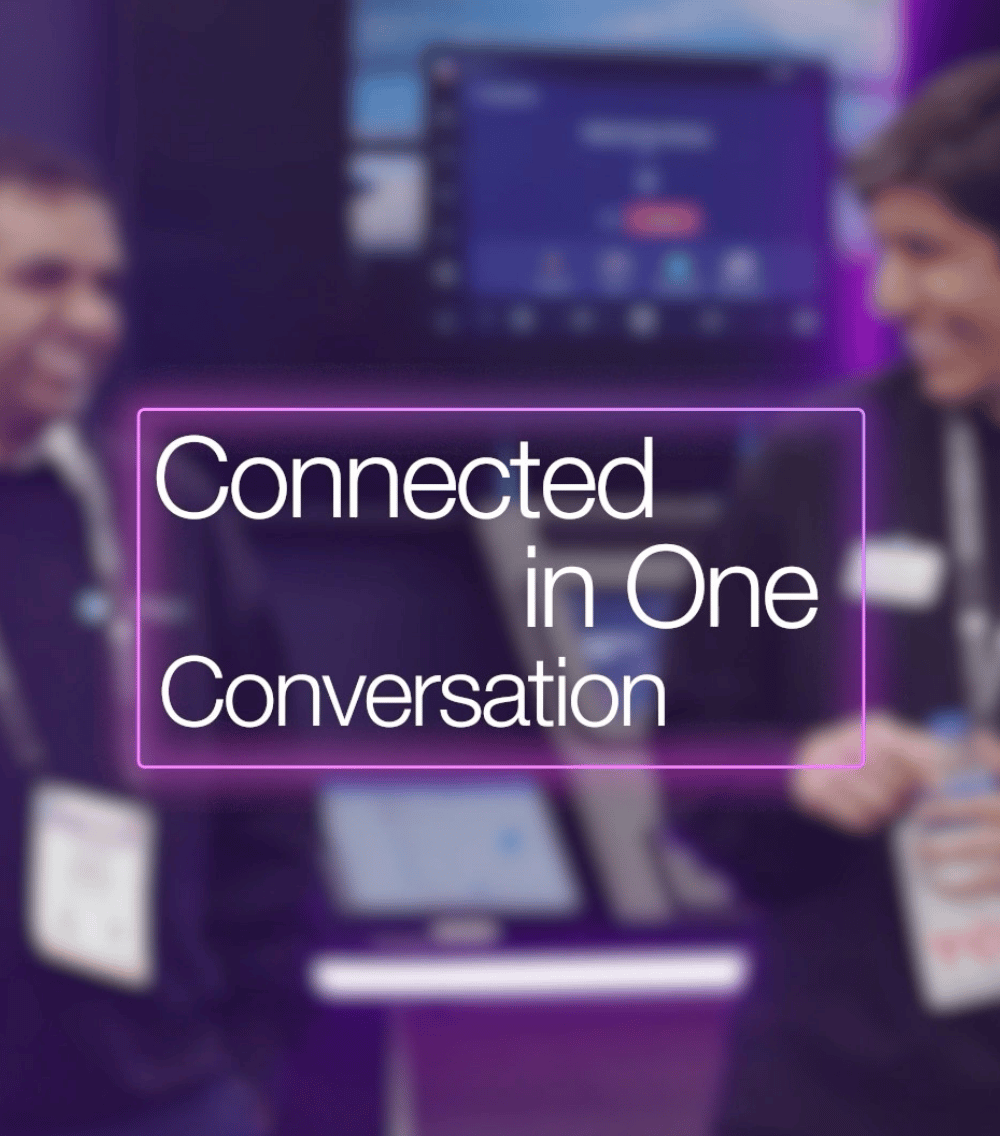 Two people facing each other and smiling with a screen in the background and the text 'Connected in One Conversation' in front